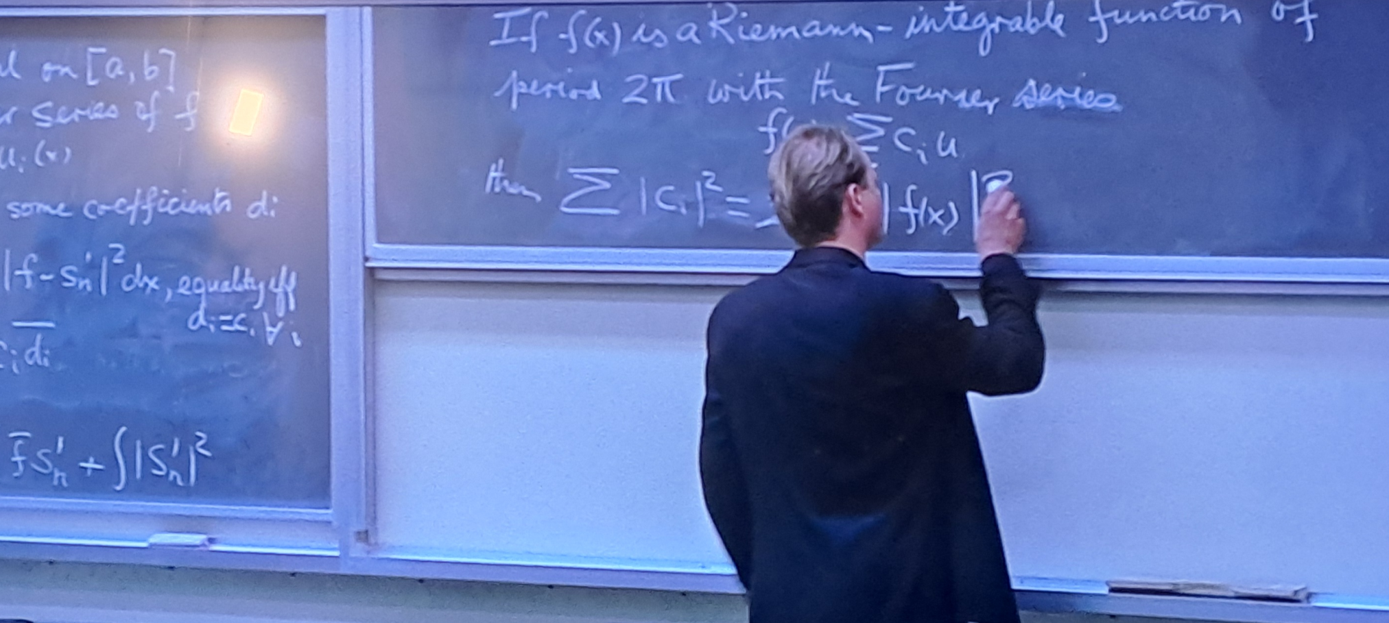Lambeau at a chalkboard containing a Fourier-series expansion and a Parseval identity.